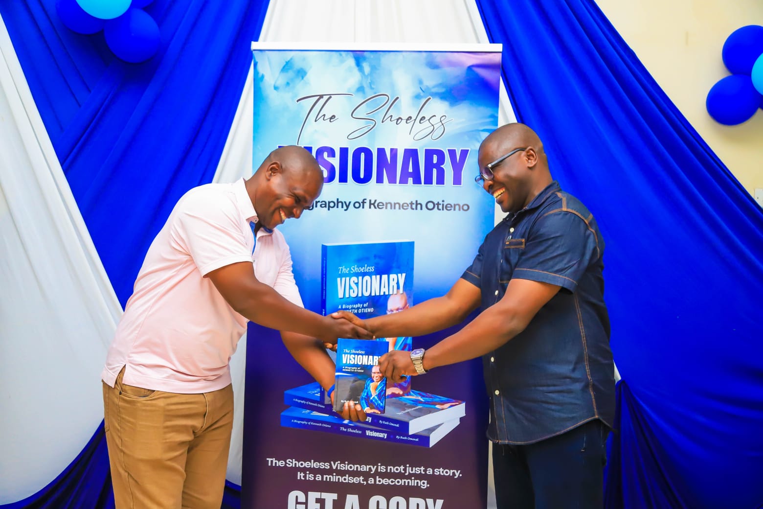 Light moment as Kenneth hands over a copy of the Biography to his first cousin George Ouma during the official launch event in Kisumu City