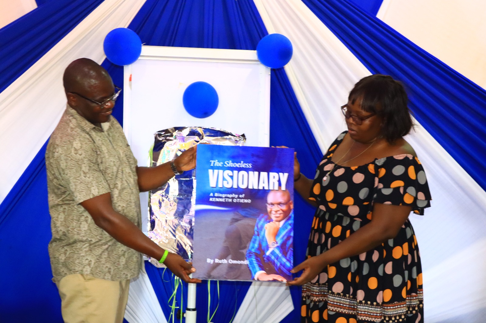 Kenneth assisted by spouse Vivian holds the dummy book at the official launch event held in Kendu Bay town venue